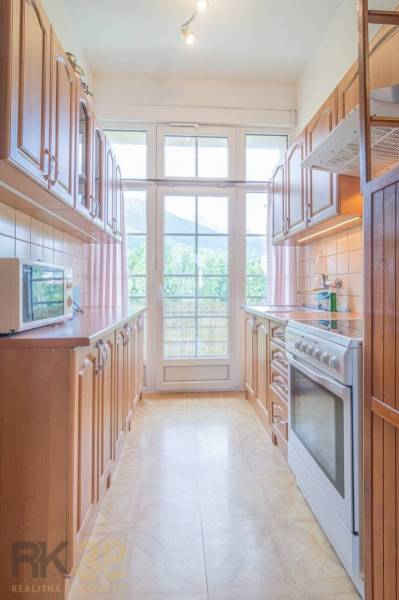 Küche mit Holzmöbeln und Geräten, Licht dringt durch ein großes Fenster ein.