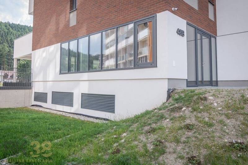 Die Fassade der Geschäftsräume in der Stadt Svit mit großen Fenstern und einem grünen Rasen.