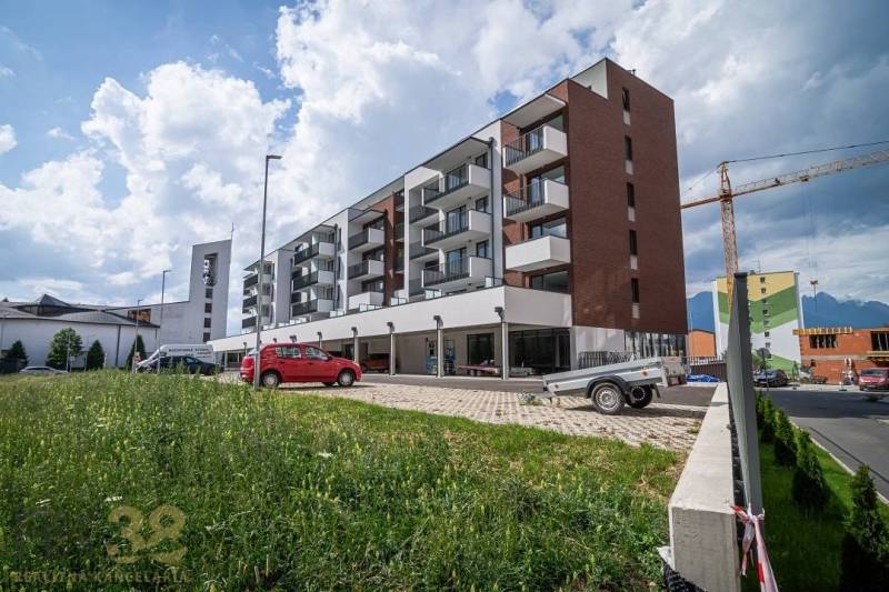Ein Gebäude in der Stadt Svit mit Geschäftsräumen und einem Parkplatz im Vordergrund.