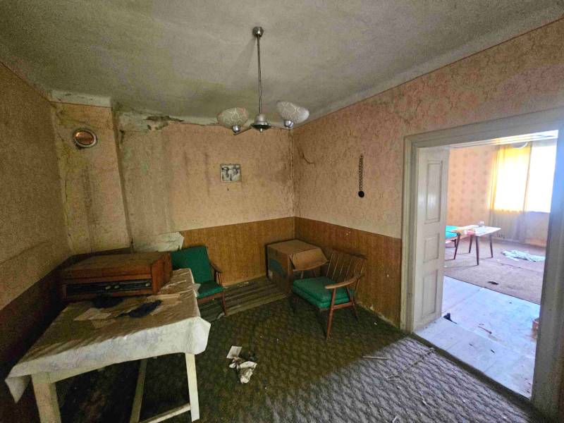 Wohnzimmer in einem Einfamilienhaus mit Retro-Möbeln und beschädigten Wänden.