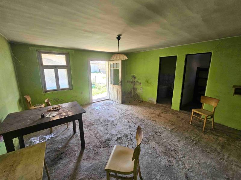Ein verlassenes Zimmer in einem Einfamilienhaus mit einfacher Einrichtung und offenen Türen nach draußen.