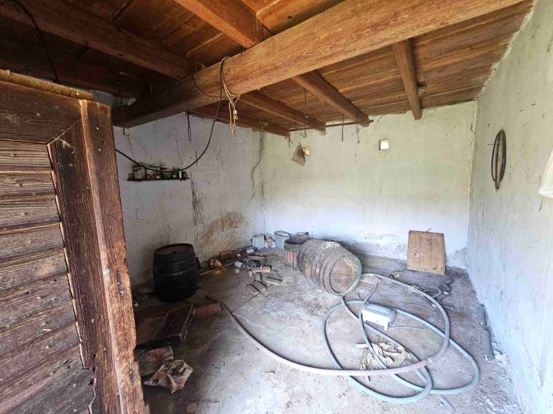 Innenraum eines Familienhauses mit einem Holzfass, alten Werkzeugen und einem Schlauch auf dem Boden.