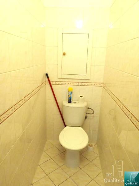 Ein kleines Badezimmer in einer Einzimmerwohnung mit Toilette, Besen und Reinigungsmitteln.