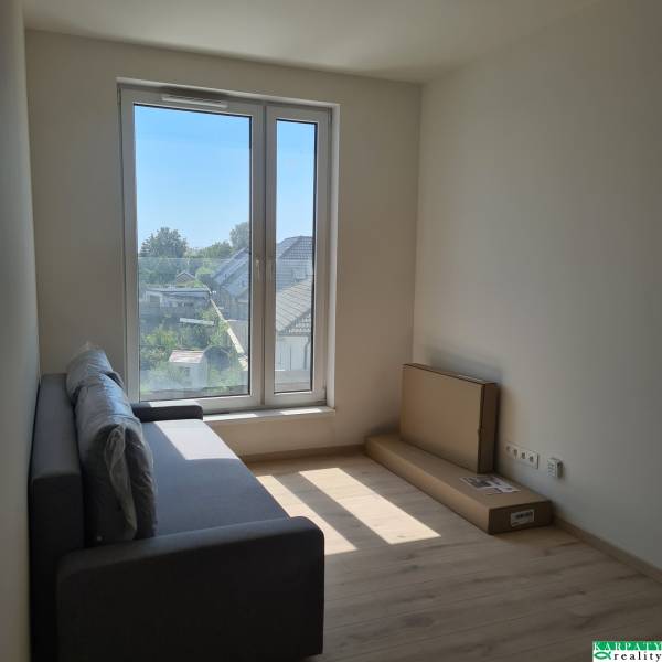 Einzimmerwohnung mit Sofa, großem Fenster und Blick auf die Häuser.