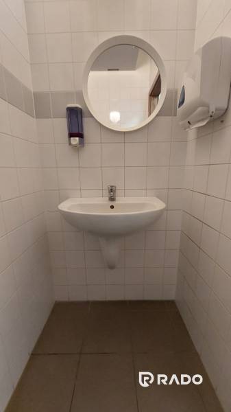 Weiße Fliesen und ein Waschbecken mit rundem Spiegel im Büro.