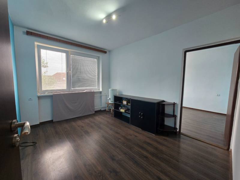 Ein Zimmer in einem Einfamilienhaus mit einem Fenster, dunkler Boden, helle Wände, Möbel an der Wand.