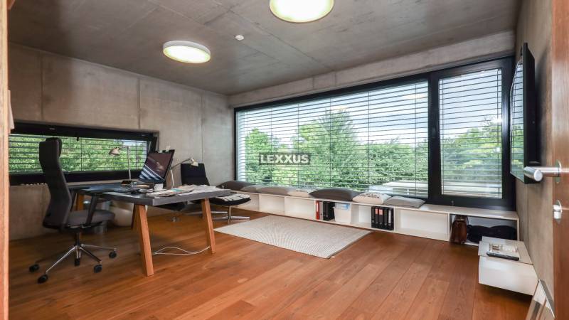 Ein Arbeitszimmer in einem Einfamilienhaus mit großem Fenster und Holzboden, moderne Möbel, Blick auf Bäume.