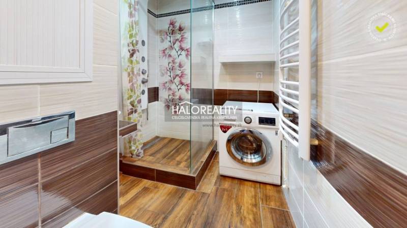 Badezimmer in einer 2-Zimmer-Wohnung mit Duschkabine, Waschmaschine und Holzverkleidung.