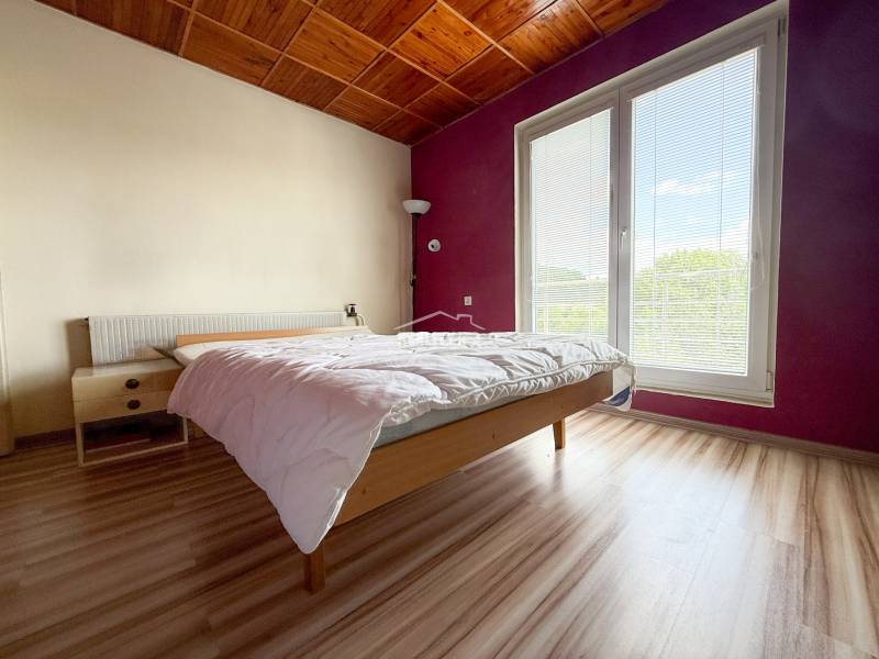 Helles Schlafzimmer in einem Einfamilienhaus mit Holzbalkendecke und großem Fenster.
