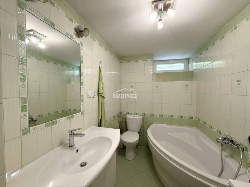Badezimmer in einem Einfamilienhaus mit Badewanne, Waschbecken und grünen Fliesen.