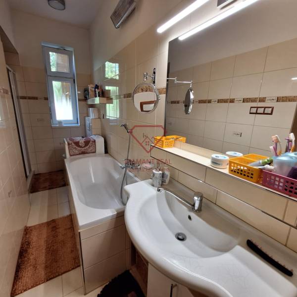 Badezimmer mit Badewanne und Spiegel in einem Einfamilienhaus, ausgestattet mit Regalen und Waschbecken.