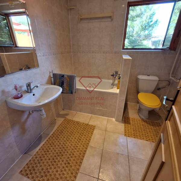 Badezimmer in einem Einfamilienhaus mit beleuchtetem Fenster, Badewanne und Waschbecken.
