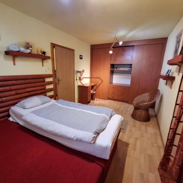 Schlafzimmer eines Einfamilienhauses mit Bett, Schrank und Rattanstuhl.