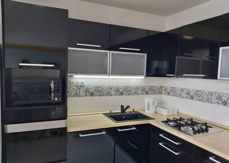 Küche in einer 3-Zimmer-Wohnung mit schwarzen Schränken, eingebautem Ofen und Gasherd.