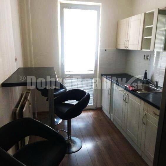 Küche in einer 2-Zimmer-Wohnung mit Bartresen, zwei Stühlen und weißen Schränken.