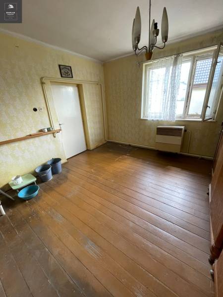 Innenraum eines Einfamilienhauses mit Holzboden, älteren Möbeln und einer hängenden Leuchte.