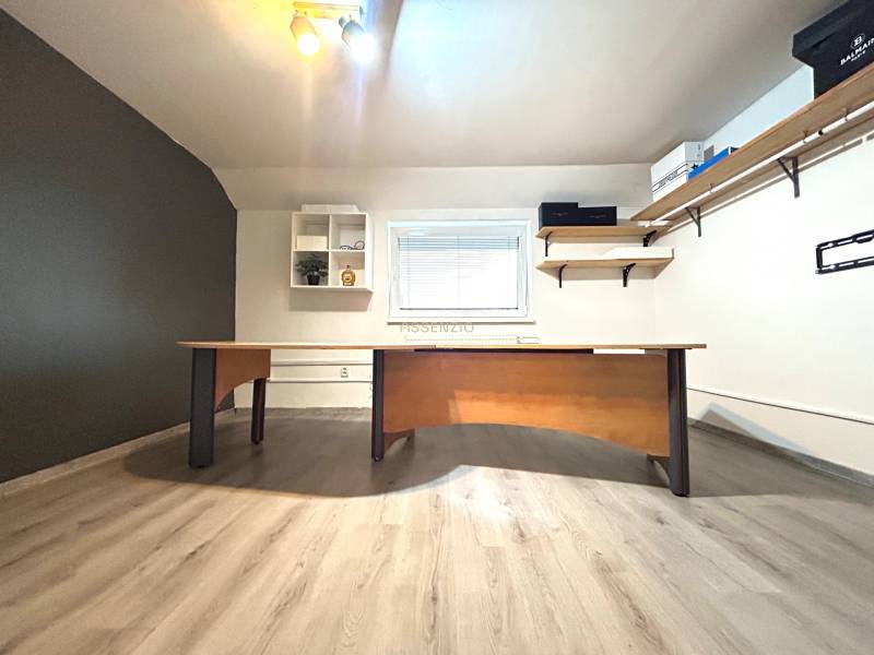 Ein Büro mit Schreibtisch und Regalen in einer 4-Zimmer-Wohnung, heller Boden, minimalistisches Design.
