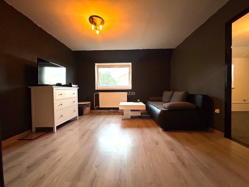 Wohnzimmer in einer Vierzimmerwohnung mit schwarzem Sofa und weißer Kommode.