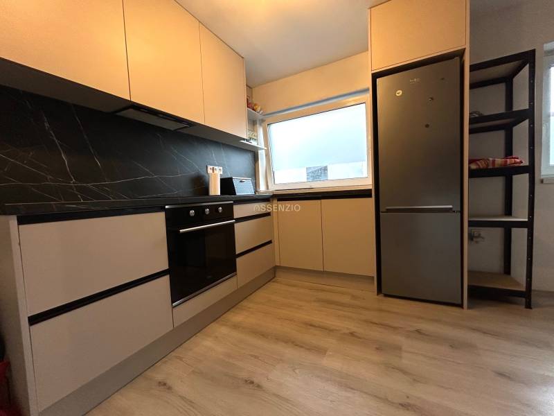 Küche in einer 4-Zimmer-Wohnung mit schwarzen Fliesen und eingebauten Geräten.