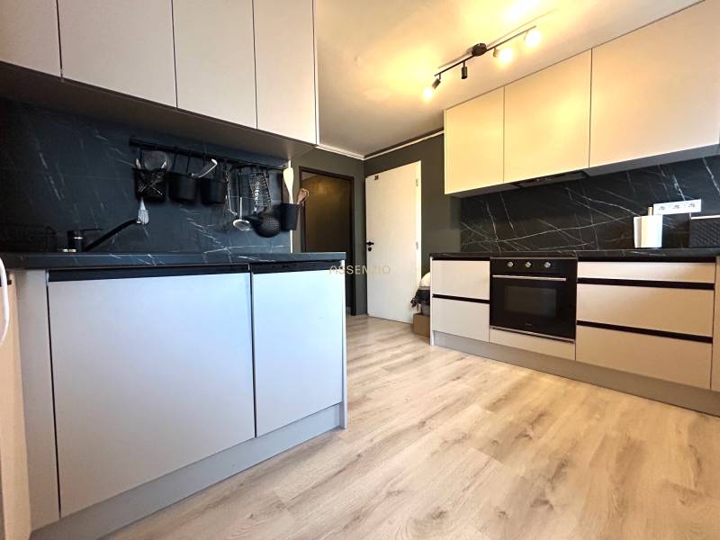 Küche mit weißen Schränken in einer 4-Zimmer-Wohnung, ausgestattet mit einer dunklen Arbeitsplatte.