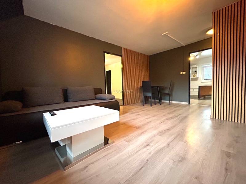 Wohnzimmer mit grauem Sofa, weißem Tisch und Essecke in einer 4-Zimmer-Wohnung.