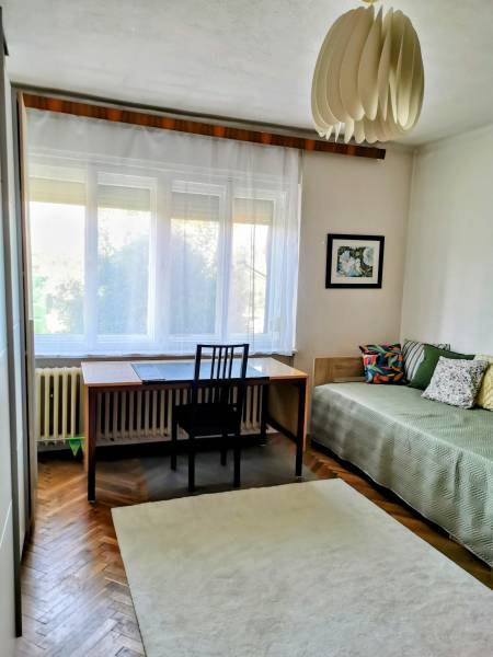 Ein Zimmer in einem Einfamilienhaus mit einem Schreibtisch, einem Bett, einem Teppich und dekorativer Beleuchtung.