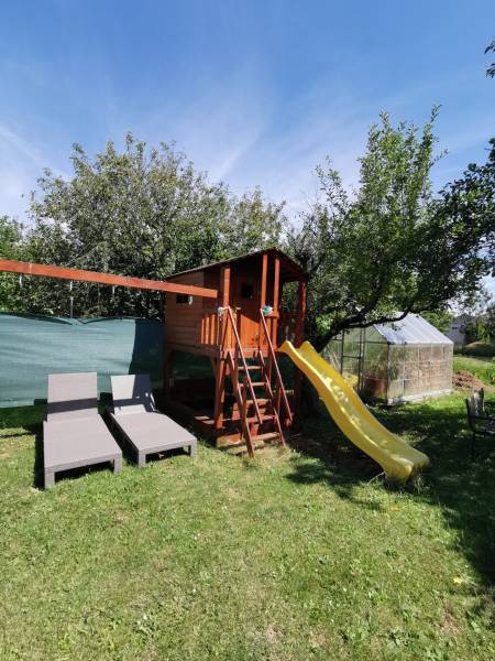 Der Garten des Einfamilienhauses in Topoľčianky mit einem Kinderspielhaus, einer Rutsche und Liegestühlen.