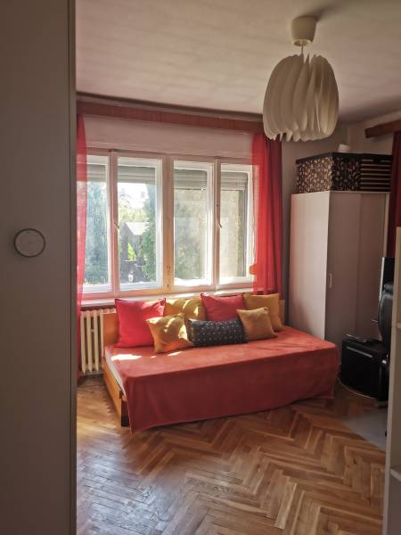Ein sonniges Zimmer in einem Einfamilienhaus mit einem orangefarbenen Sofa, Kissen und Holzboden.