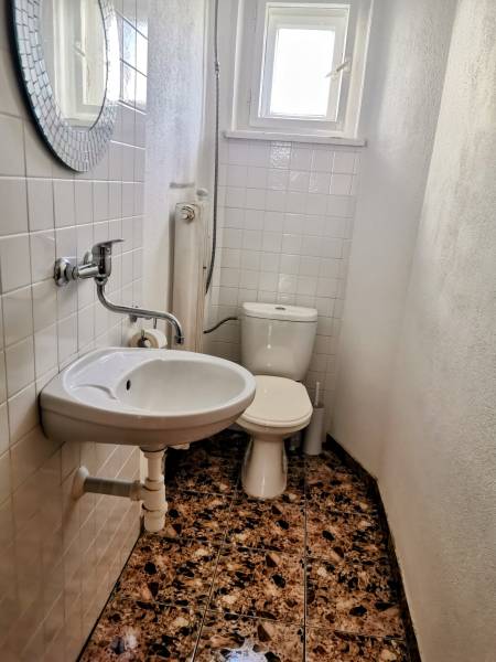 Badezimmer in einem Einfamilienhaus mit Waschbecken, Toilette und Fenster, weiße Fliesen an den Wänden.