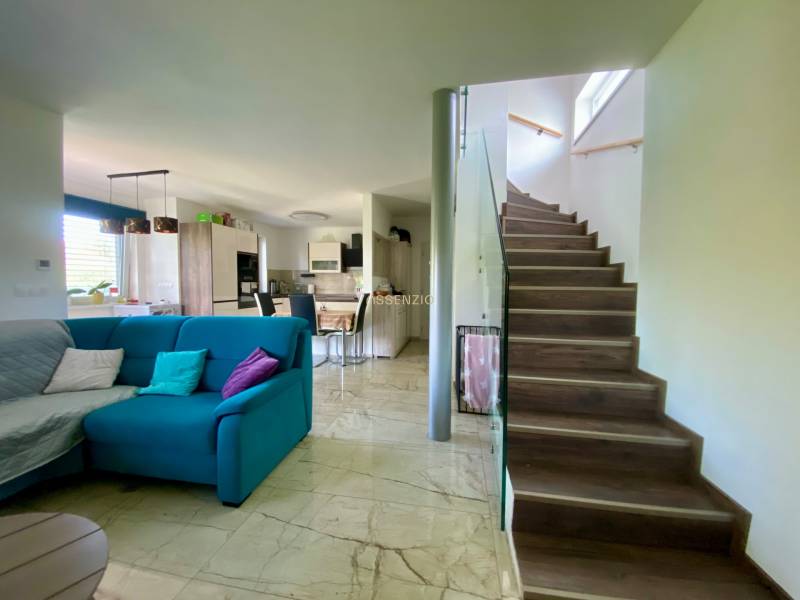 Wohnzimmer mit Küche in einem Einfamilienhaus, Treppe, bequeme Couch und Esstisch.