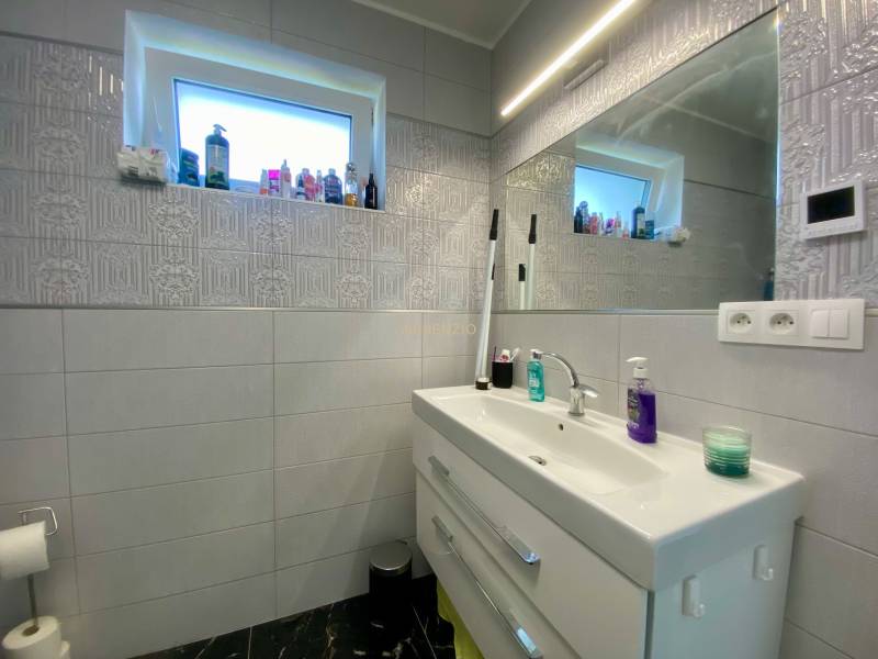 Badezimmer in einem Einfamilienhaus mit Waschbecken, Spiegel und viel Kosmetik.
