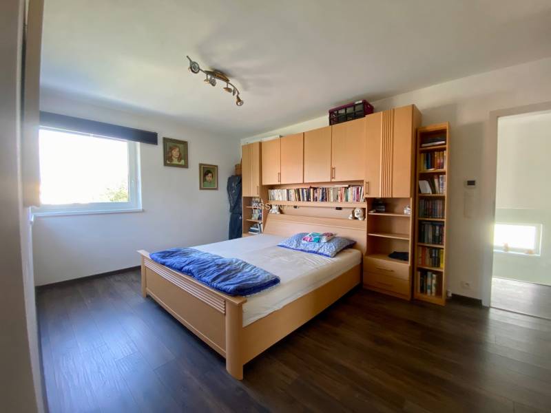 Schlafzimmer mit Bett, Holzmöbeln und Bücherregal in einem Einfamilienhaus.