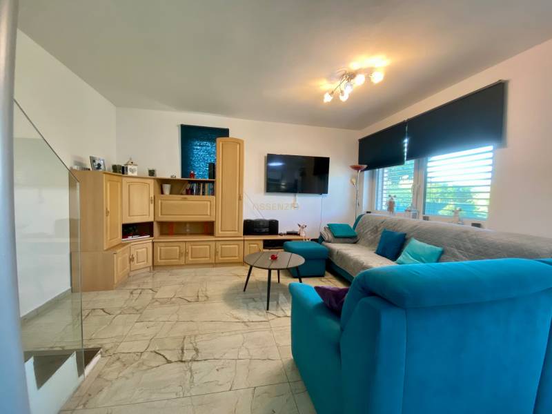 Wohnzimmer mit hellem Boden, Holzschrank und blauem Sofa in einem Einfamilienhaus.