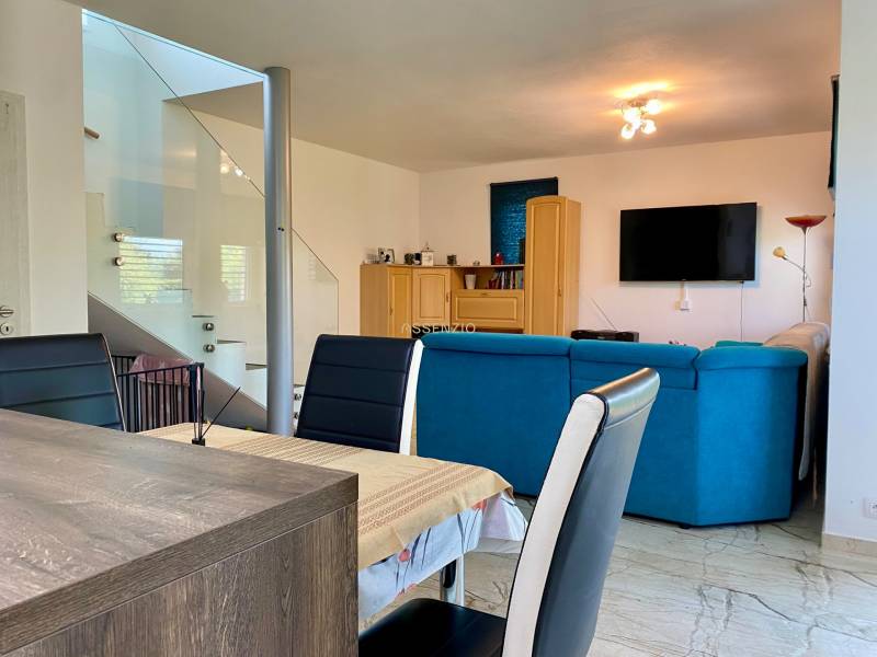 Wohnzimmer in einem Einfamilienhaus mit einem blauen Sofa, einem Esstisch und einem Fernseher an der Wand.