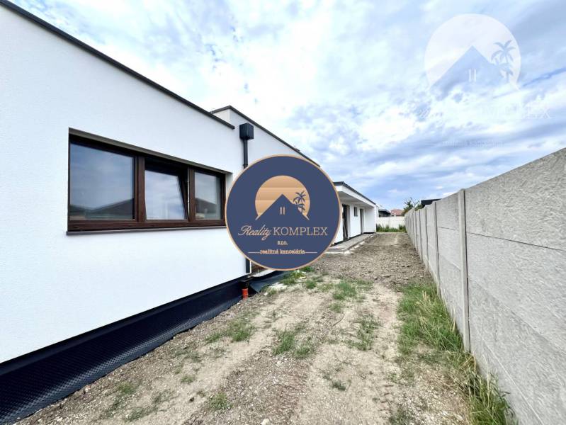 Ein Einfamilienhaus in Miloslavov mit weißer Fassade, daneben steht ein Zaun und eine Straße.