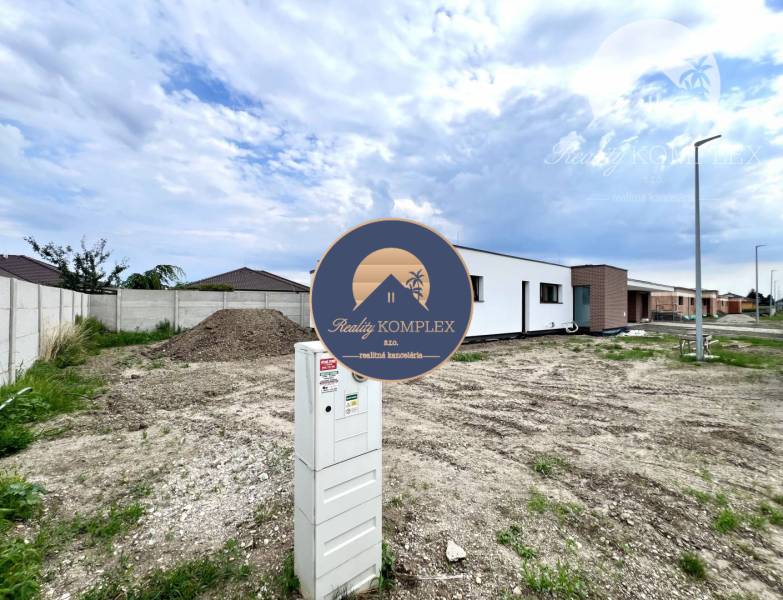 Baugrundstück neben einem Einfamilienhaus in Miloslavov mit sichtbarem Stromverteiler und Betonzaun.