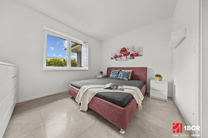 Schlafzimmer im Einfamilienhaus mit Doppelbett, Blumenbild und Nachttischen.