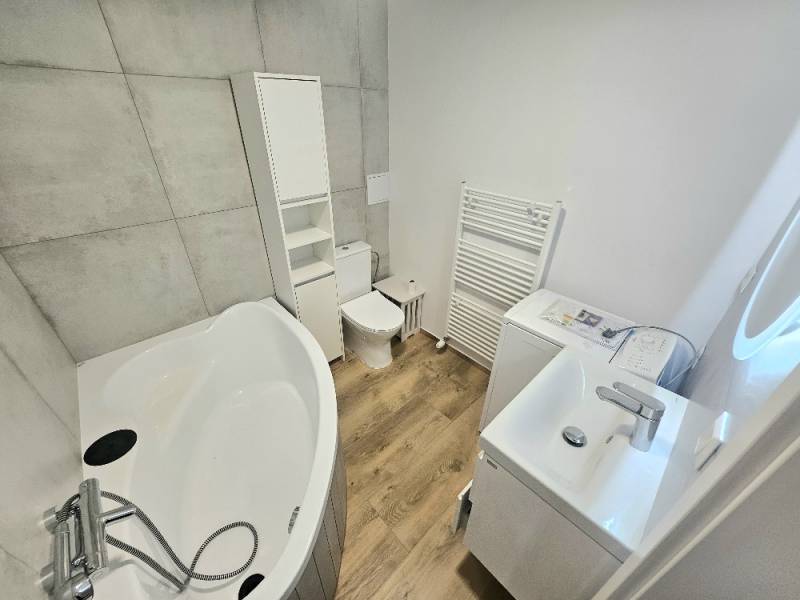 Badezimmer mit ovaler Badewanne, Toilette und Waschmaschine in einer Einzimmerwohnung.