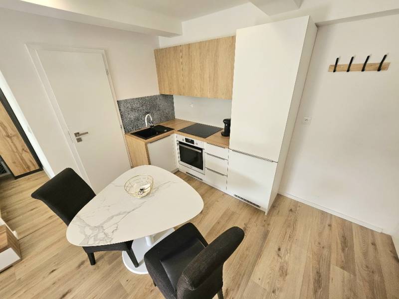 Küche in einer Einzimmerwohnung mit Holzboden, Esstisch und weißen Schränken.
