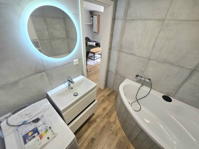 Badezimmer mit Badewanne, Waschbecken, Waschmaschine und LED-Beleuchtung in einer Einzimmerwohnung.