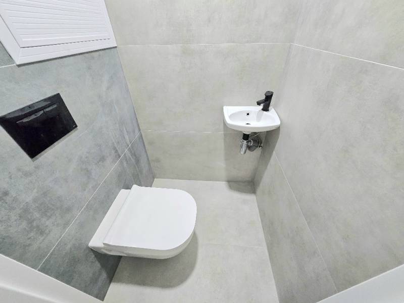 Badezimmer in einer 3-Zimmer-Wohnung mit Toilette und Waschbecken, gefliest mit grauen Fliesen.