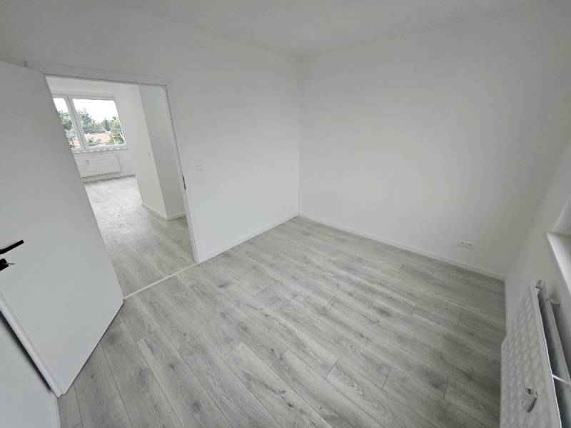 Ein heller Raum in einer 3-Zimmer-Wohnung mit Laminatboden und offenen Türen.