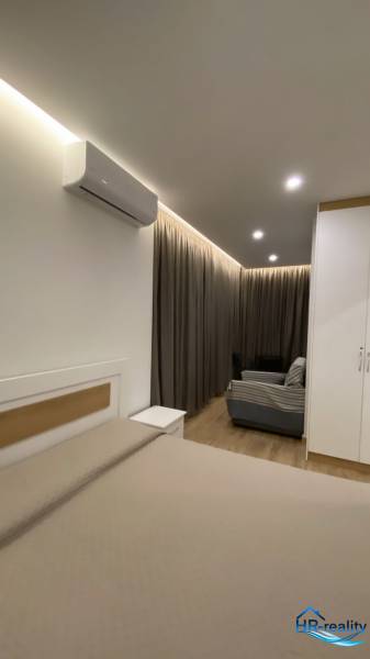 Innenraum einer Ferienwohnung mit Bett, Sofa, Vorhängen und Klimaanlage.