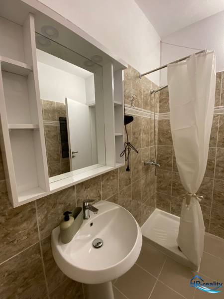 Badezimmer in einer Ferienwohnung mit Waschbecken, Duschkabine und Spiegel mit Ablagen.