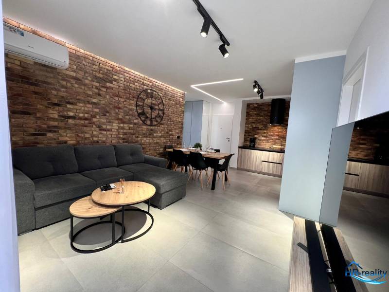 Wohnzimmer in einer Ferienwohnung mit Ziegelwand, Sofa und Fernseher.