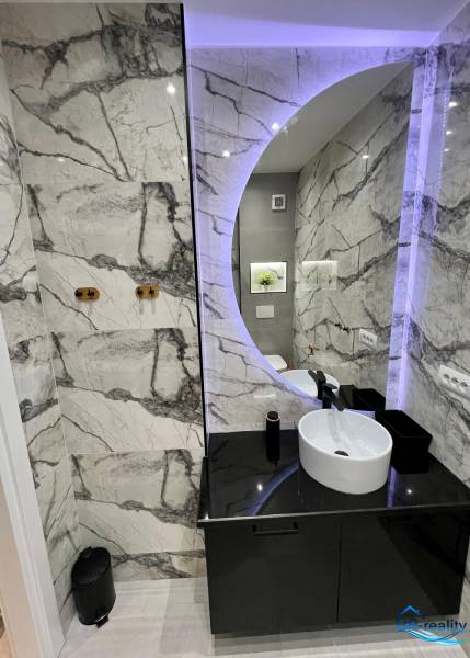 Badezimmer in der Ferienwohnung mit rundem Spiegel und eleganten Fliesen.