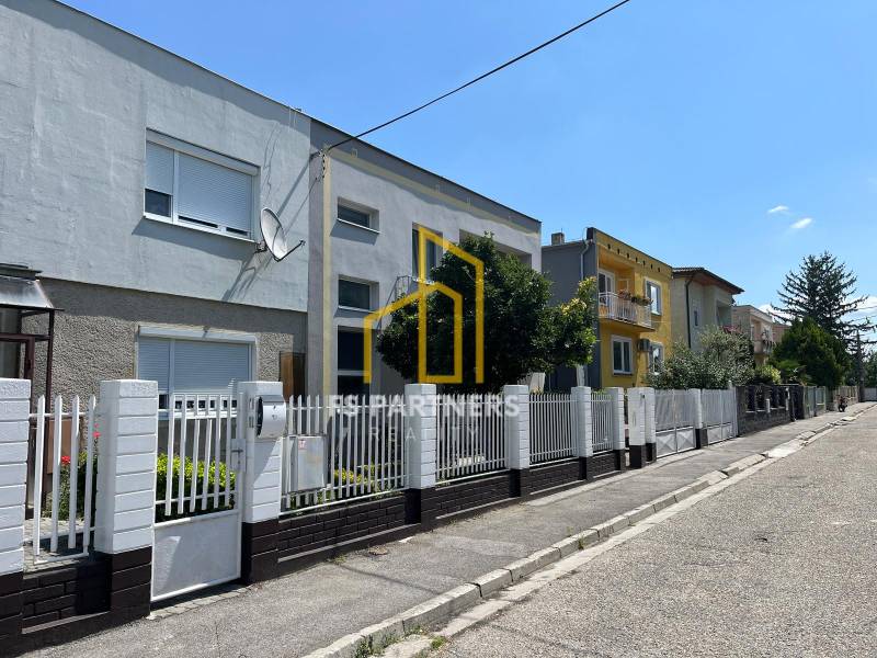 Eine Straße mit Einfamilienhäusern in Komárno, mit einem weißen Zaun und einer Satellitenschüssel.
