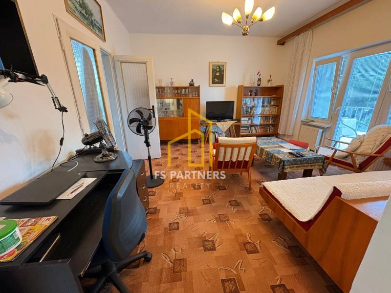 Wohnzimmer in einem Einfamilienhaus mit älteren Möbeln und einem Tischventilator.