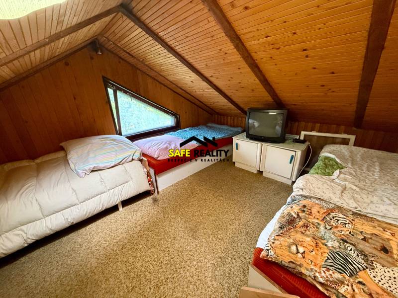 Dachzimmer in einer Hütte mit drei Betten und einem Fernseher.