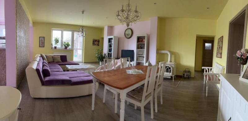 Wohnzimmer in einem Einfamilienhaus, helle Wände, großes lila Sofa, Esstisch.